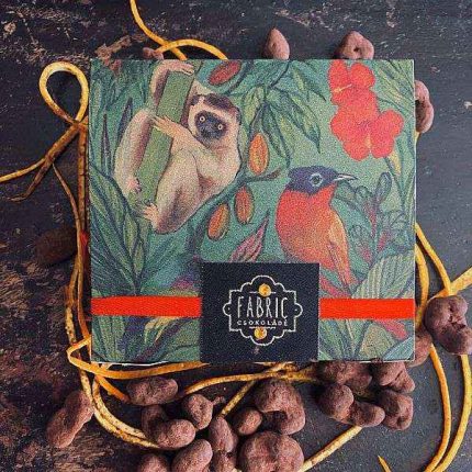 Obal čokolády Fabric s ilustrací opice a barevného ptáka na zeleném pozadí.